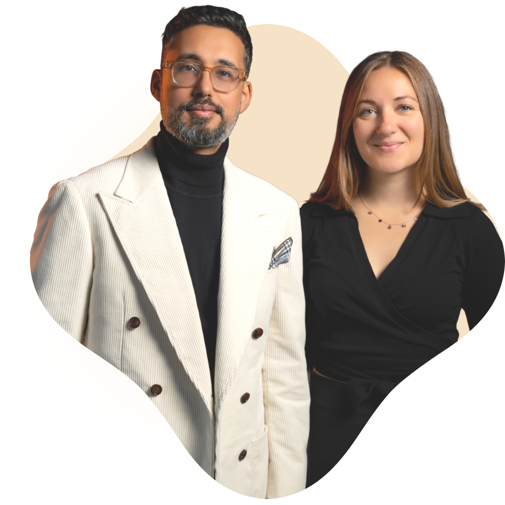Variant12 A man in a white double-breasted suit and glasses stands next to a woman in a black wrap dress, both smiling at the camera, representing confidence and vitality often seen in those benefitting from an executive health program.