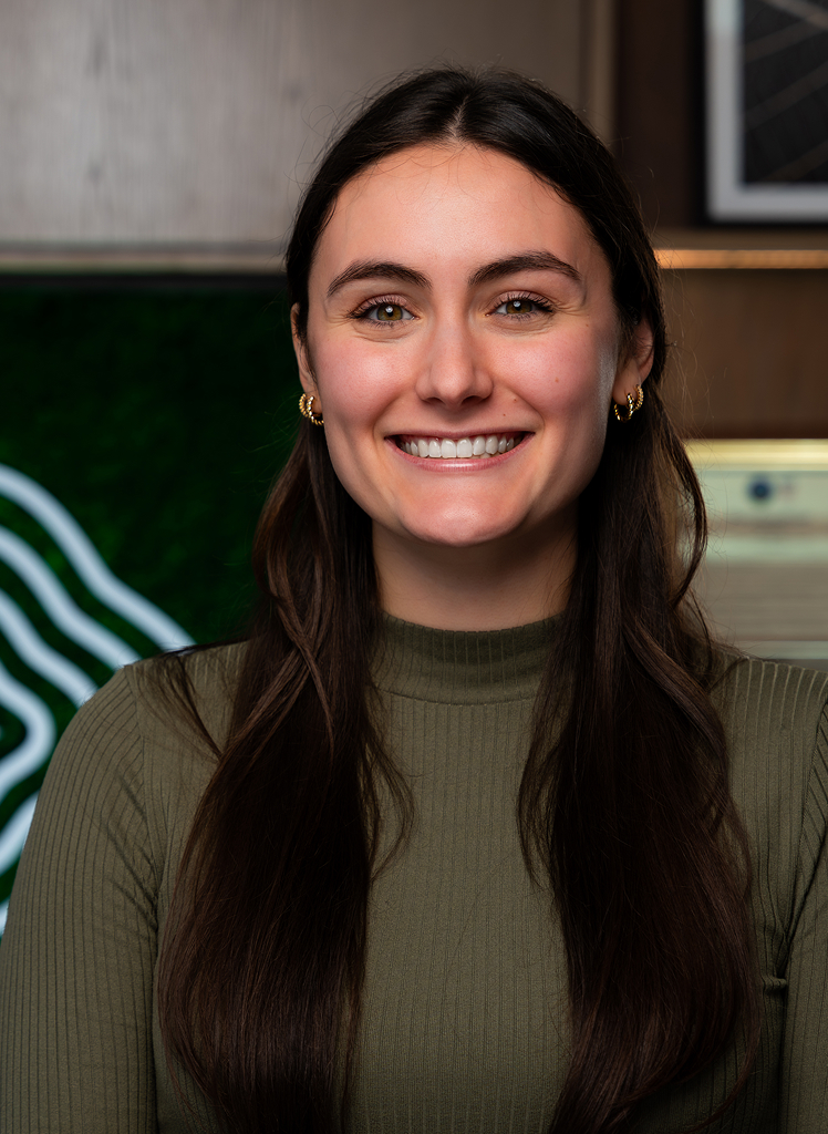 Frame 882_1 Tori Bradley smiles at the camera. She is wearing a green ribbed top and stands indoors with a blurred background.